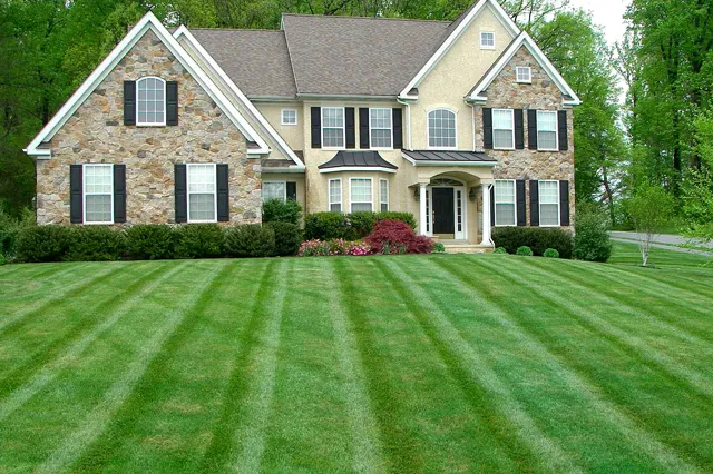 Perfectly striped and densely maintained residential lawn in front of a stone and stucco estate home