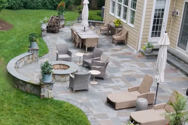 Aerial view of a bluestone patio with curved fieldstone seat wall, fire pit, and outdoor living areas adjacent to a Chester County estate, designed and built by Eastern Horticultural Services
