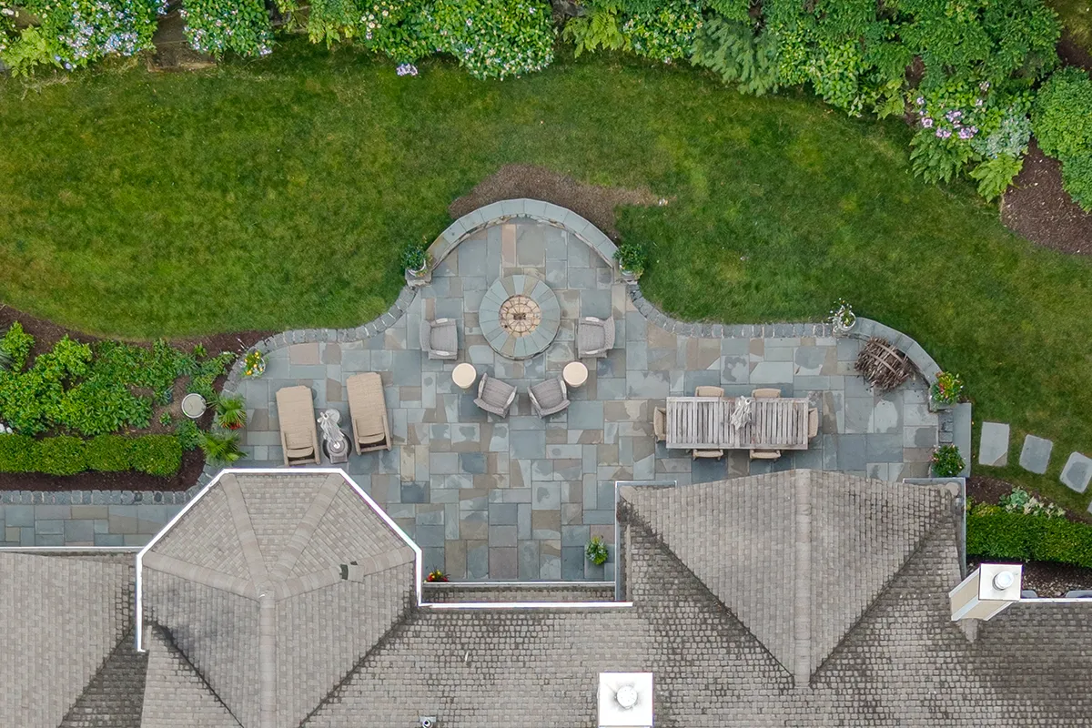 Aerial view of a custom landscape design-build project in Kennett Square, Pennsylvania, featuring a circular brick paver entry garden with curved planting beds and a bluestone patio with fire pit