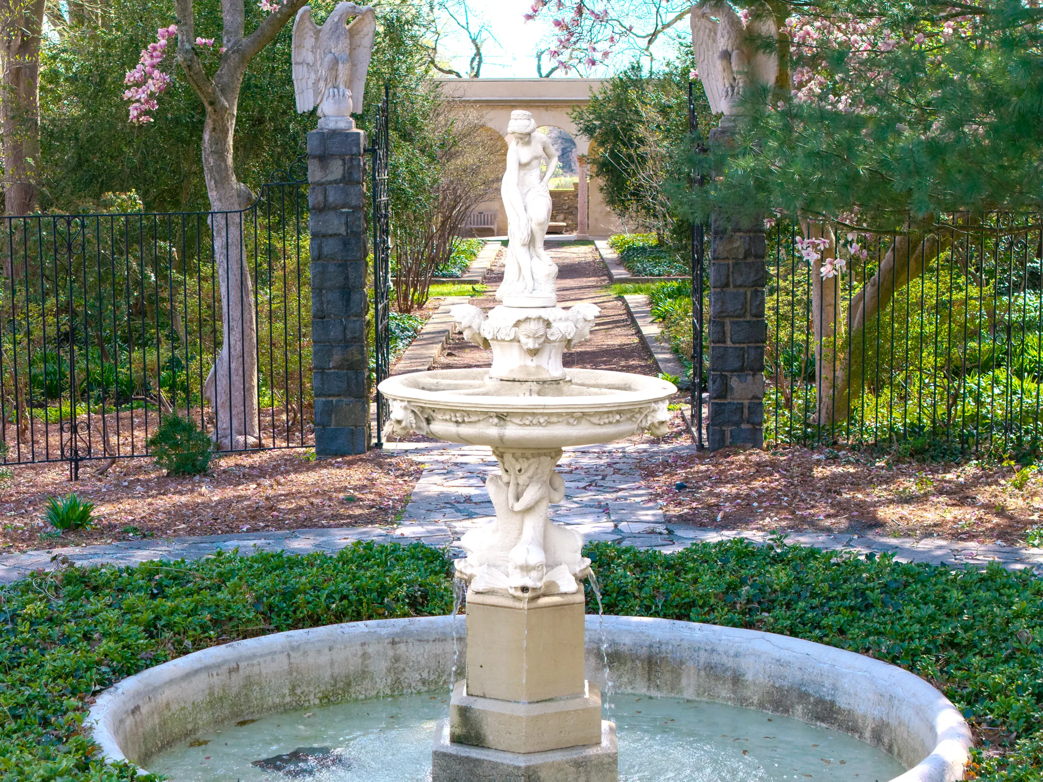 Classical two-tiered marble fountain on the formal garden axis, framed by iron gates with eagle-topped Brandywine granite pillars, saucer magnolias in bloom, Gibraltar Estate, Wilmington, DE