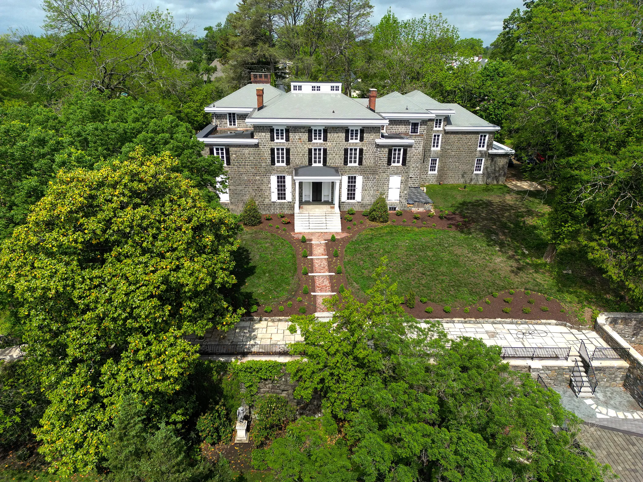 Aerial view of restored Gibraltar Estate mansion and grounds in spring 2025 showing new plantings, brick entry approach, and cleared landscape