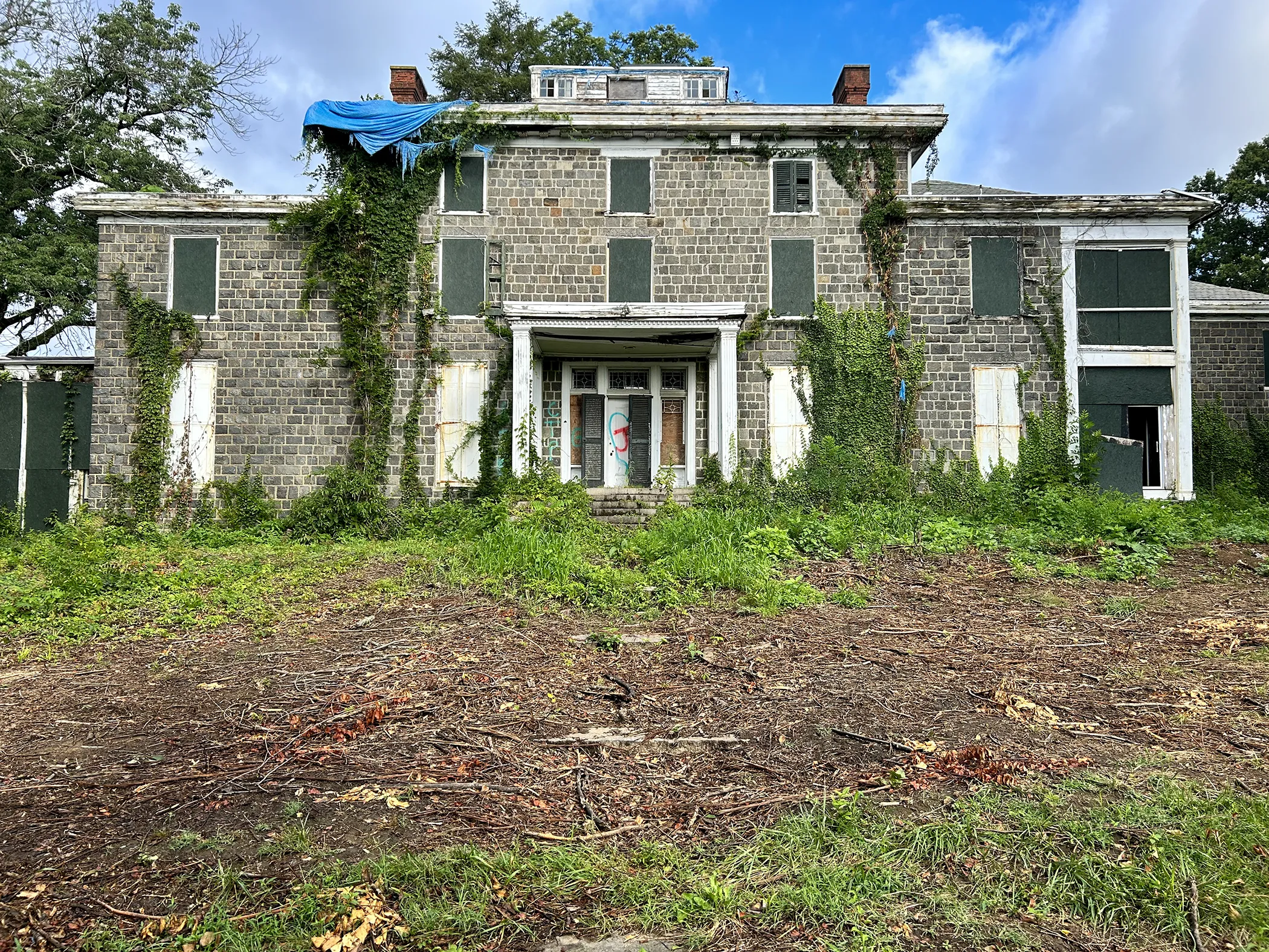 Gibraltar Estate mansion facade before restoration showing vine overgrowth, boarded windows, and abandoned condition