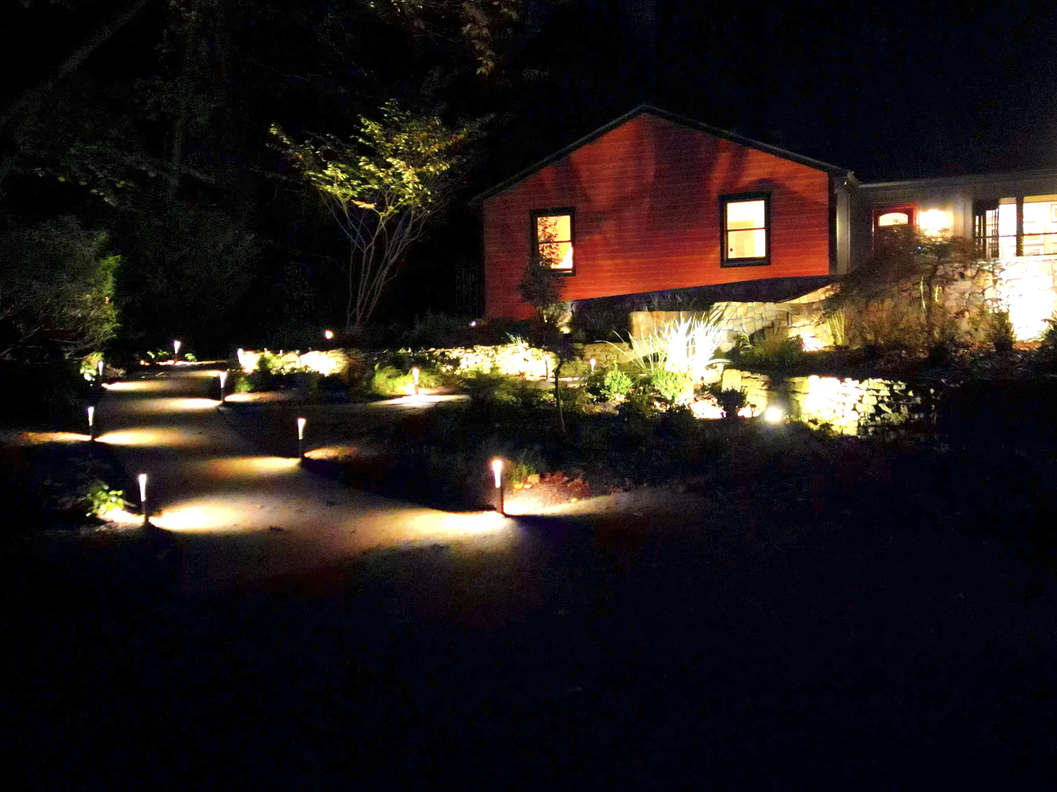 Nighttime view of lit path leading toward North Star residence with landscape lighting on stepping stones, retaining walls, and plantings
