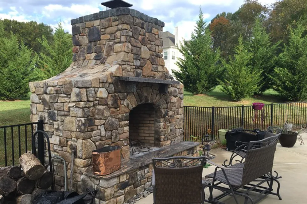 Custom outdoor fieldstone fireplace with brick firebox and stone hearth — custom masonry by Eastern Horticultural Services