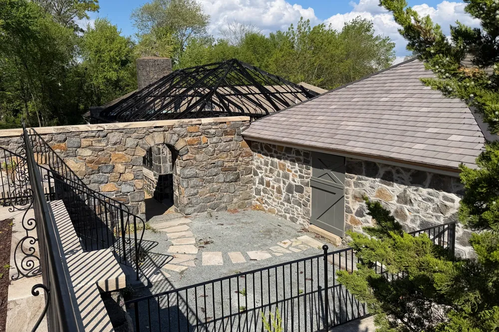 Historic stone carriage house under restoration with reconstructed fieldstone walls and exposed roof structure — masonry restoration by Eastern Horticultural Services, Gibraltar Estate, Wilmington DE