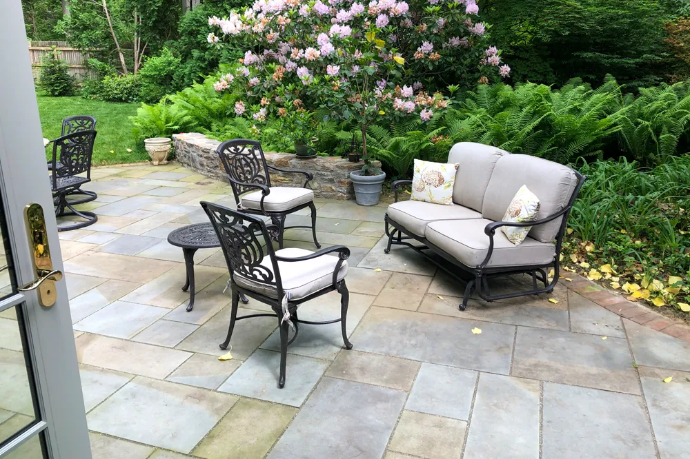 Wet-laid bluestone patio with outdoor seating, Rhododendron border, and fieldstone garden wall — masonry by Eastern Horticultural Services, Kennett, PA