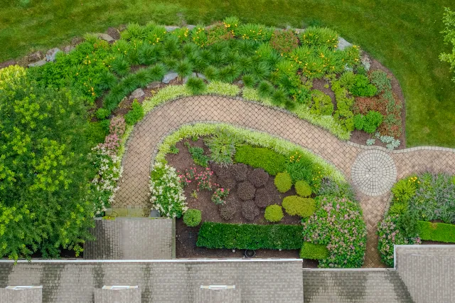 Aerial view of a formally designed garden with curved brick paths, layered mixed planting beds, ornamental grasses, and perennials — landscape installation by Eastern Horticultural Services, Chester County PA