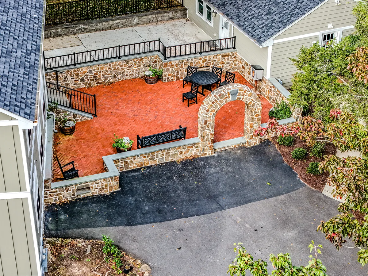 Dry-laid irregular fieldstone patio with crushed stone joints, low stone planter wall, and specimen plantings including a red Japanese maple