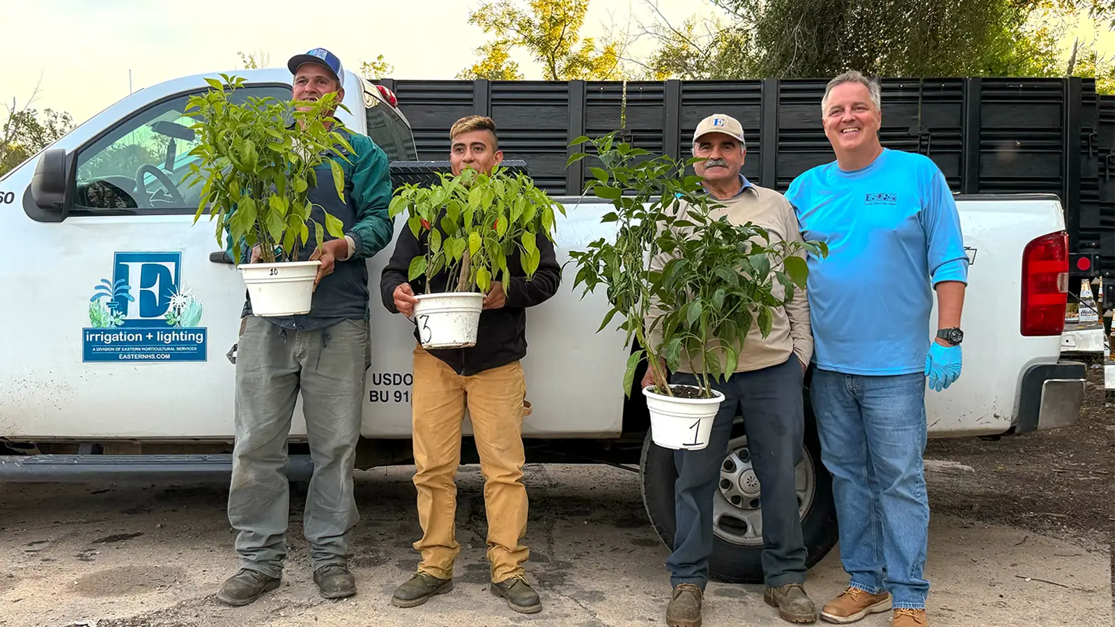 Three EHS team members holding potted jalapeño plants beside John Winterbottom in front of an EHS truck in Avondale