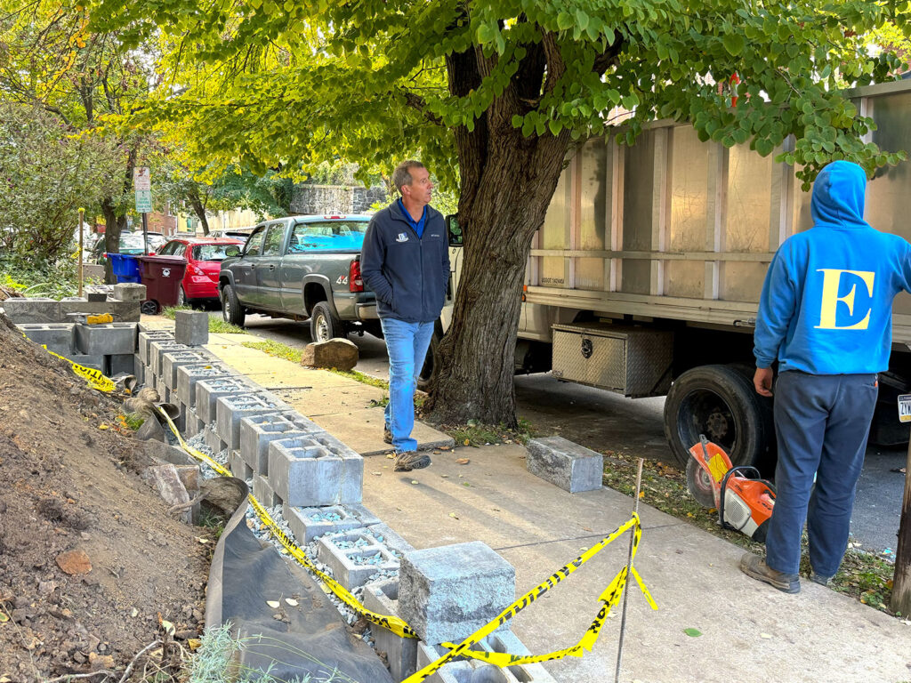 EHS crew building a Diamond Pro retaining wall along a city sidewalk, stone-filled block cores and filter fabric visible
