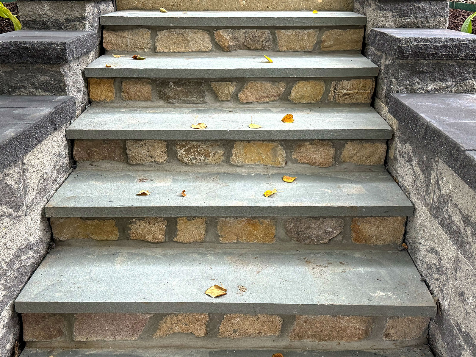 Rebuilt front steps with bluestone treads over fieldstone risers, framed by capped retaining wall pillars