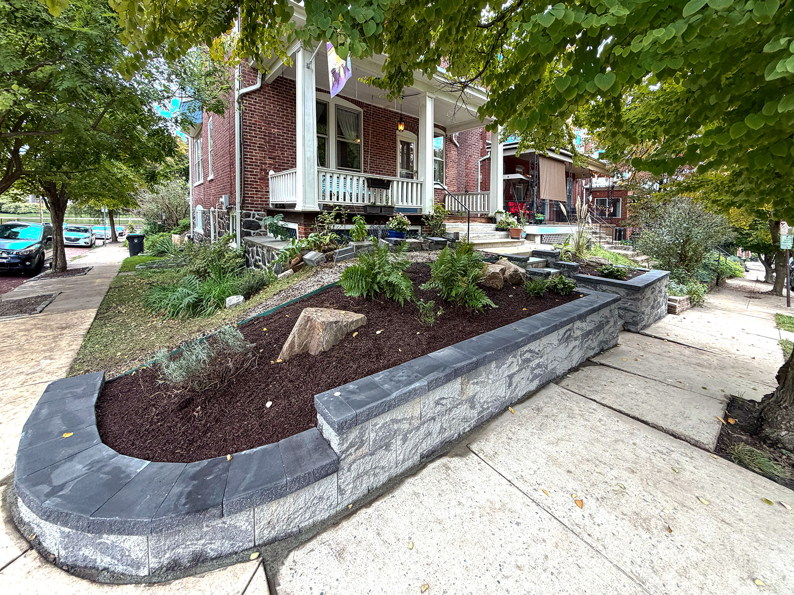 Curved Belgard retaining wall with dark cap course turning the corner of a city lot, new planting bed behind